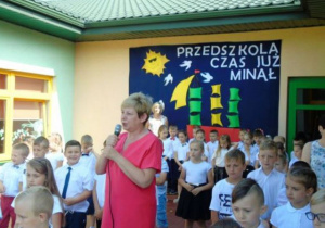 Kobieta przemawia przez mikrofon, dzieci w tle