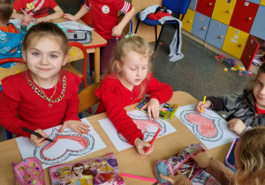Cztery dziewczynki siedzą przy stoliku i kolorują kolorowankę - serce.