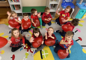 Grupa dzieci pozuje do zdjęcia trzymając w rękach czerwone balony w kształcie serca.
