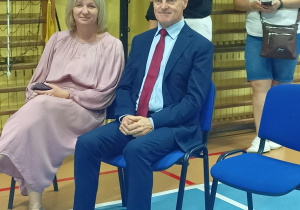 Na krzesłach siedzi kobieta i mężczyzna, za nimi stoją dwie kobiety.
