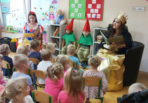 Grupa dzieci słucha baśni czytanej przez Królewnę Śnieżkę i złą Królową.
