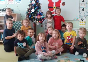 dzieci siedzą na dywanie przy świątecznie ubranej choince