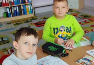 chłopcy siedzą przy stoliczku i kolorują kolorowankę Mikołaja