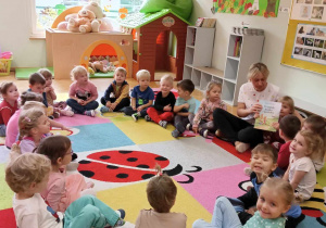Dzieci siedzą w kole z panią wychowawczynią.