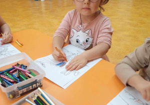 Dziewczynka siedzi przy stoliku i koloruje rysunek.