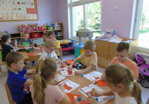 Przy stolikach siedzą dzieci i wykonują flagi z wydzieranki.