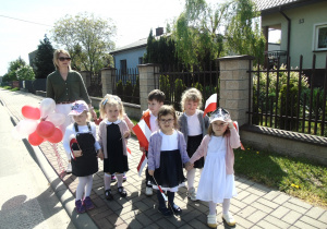 Dzieci trzymające w rączkach flagę idą na spacer z panią opiekunką.