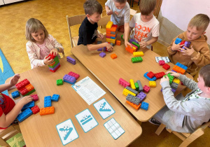 Przy stolikach siedzą dzieci i układają klocki.