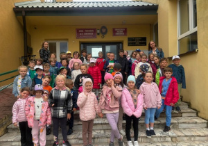 Grupa przedszkolaków wraz z dwiema nauczycielkami przed wejściem do budynku szkoły podstawowej.