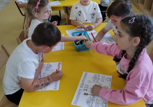 Przedszkolaki kolorujące przy stoliku obrazki dotyczące numerów alarmowych.