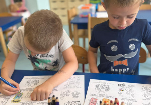 Dwaj chłopcy kolorujący obrazki dotyczące bezpiecznych wakacji.