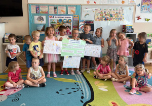 Grupa przedszkolaków trzymająca plakat wskazujący, jak należy zachować się w trakcie burzy i silnego wiatru.