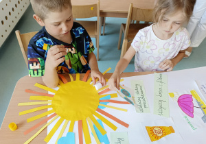 Chłopiec wraz z dziewczynką siedzący przy stoliku i przygotowujący plakat.