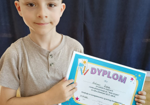 Chłopiec prezentujący dyplom otrzymany za udział w zajęciach z koła plastycznego.