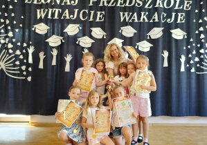 Grupa dziewczynek wraz z opiekunką, prezentujących otrzymane dyplomy, medale i puchar.